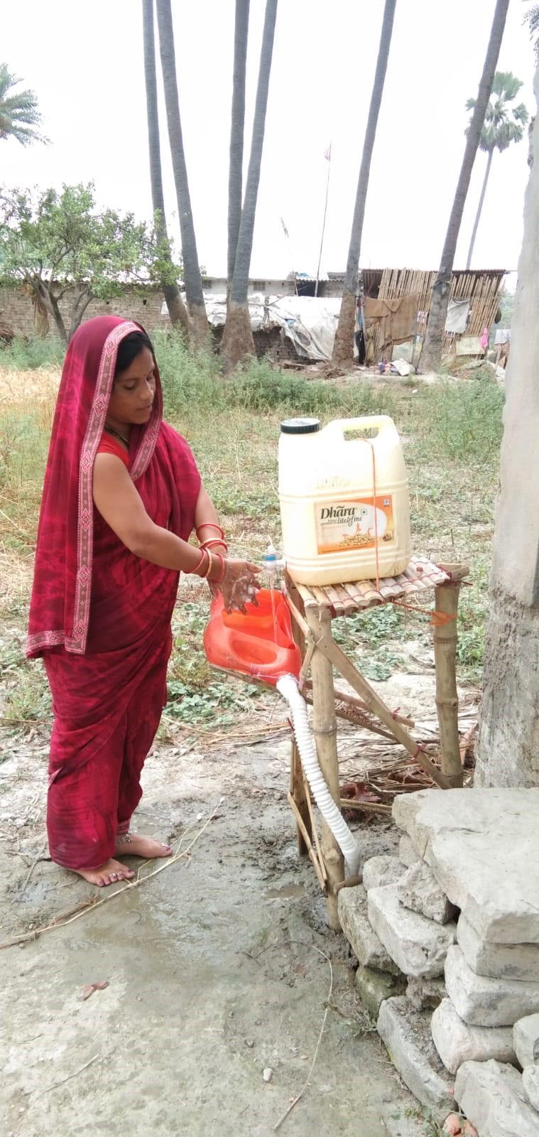A woman washing hands on the bamboo stick low cost handwashing station (Image Source: Sehgal Foundation)