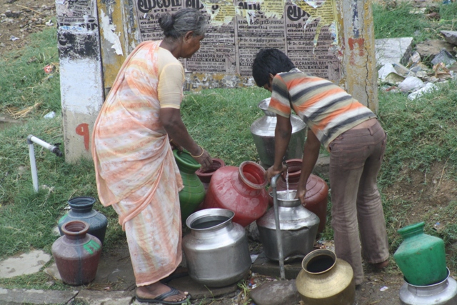 Filling their pots from a public standpost, from a thin water flow
