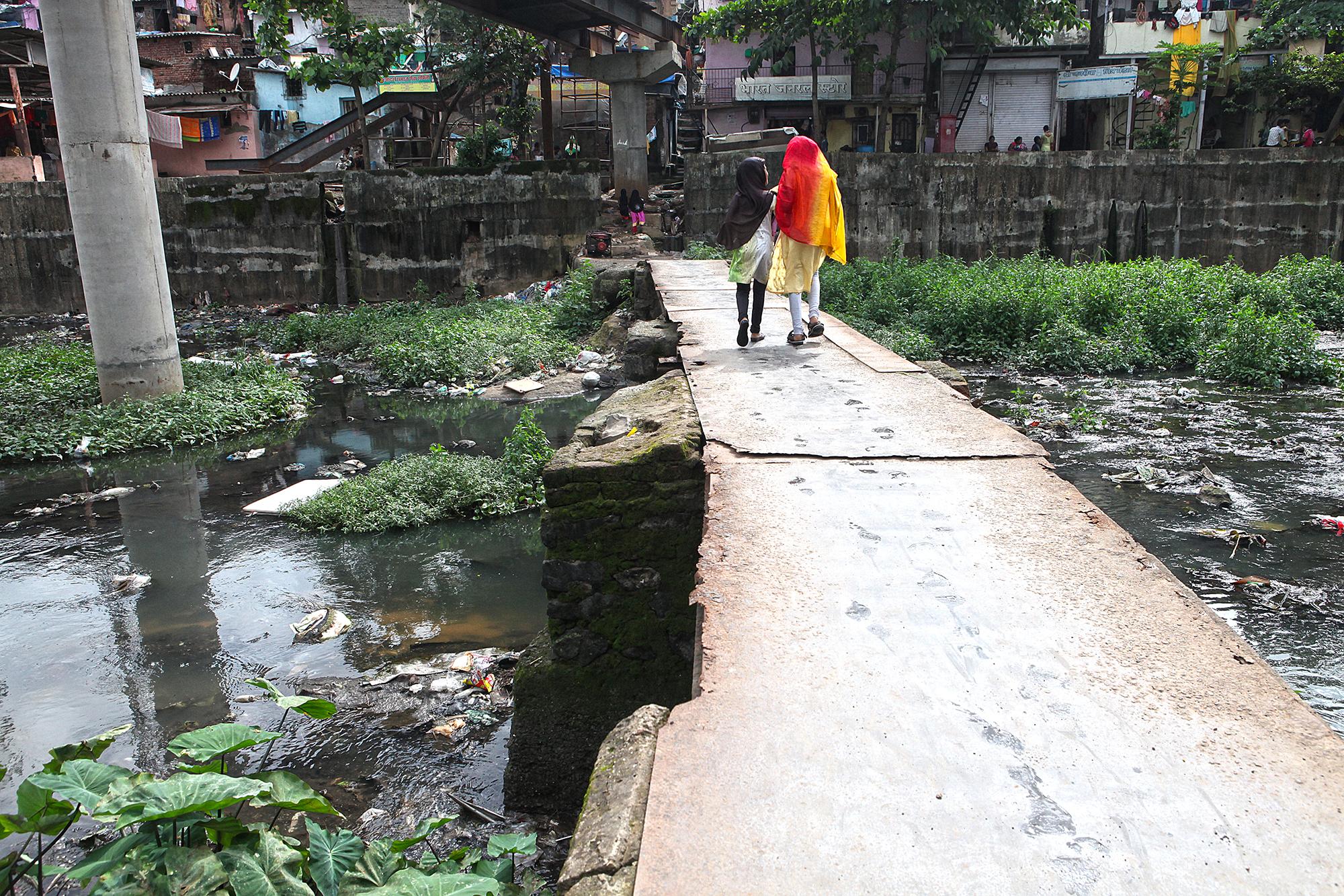 Two young girls walk on the makeshift bridge over the Mithi river at Bhim Nagar