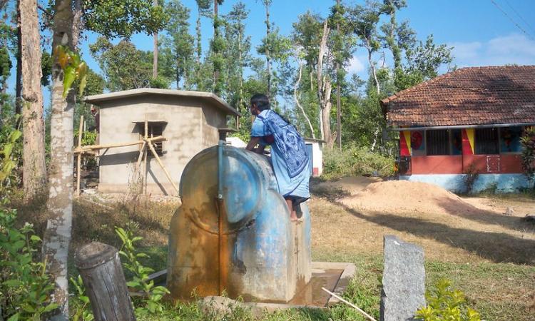 A woman climbs up a water tank to fetch water due to lack of access to pipe water connection (Image Source: India Water Portal Flickr Album)