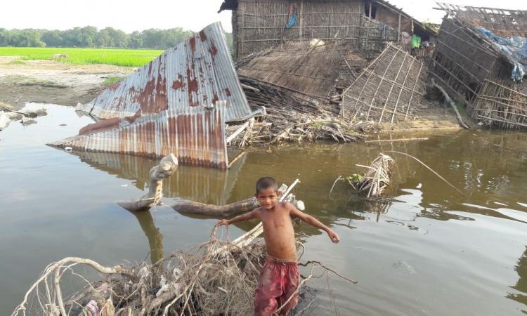 A boy stands in front of houses destroyed by flood in Karimganj district, Assam.