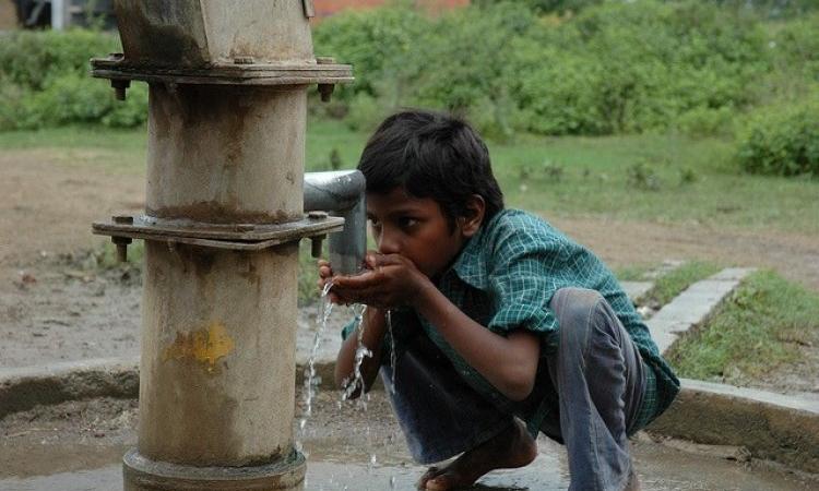 A child drinks water from a hand pump. (Image Source: IWP Flickr photos)